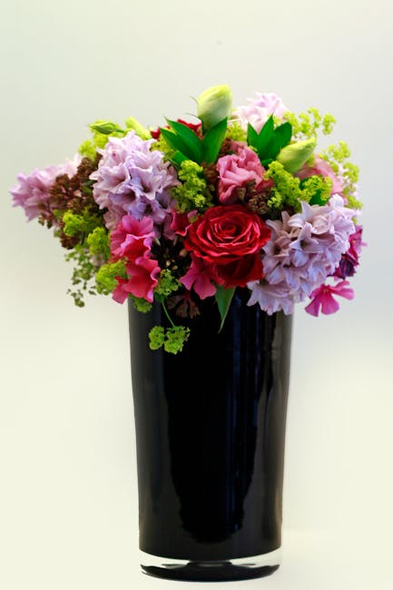 A vibrant floral arrangement featuring a mix of pink, red, and purple flowers, including a prominent red rose at the center, surrounded by pink and purple lisianthus and green foliage, all arranged in